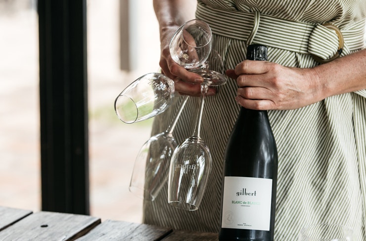 A person clutching a bottle of sparkling wine and champagne flutes